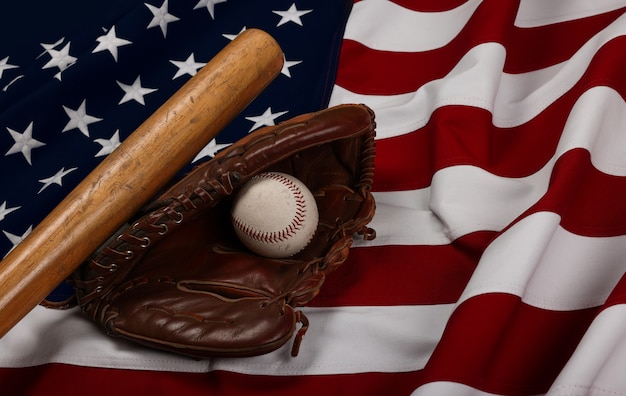 Feche a velha bola de beisebol, o taco de madeira e a luva vintage de couro desgastado no fundo da bandeira americana, vista de alto ângulo