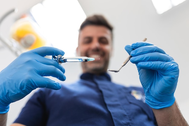 Feche a visão dos pacientes de um dentista Bonito dentista em luvas cirúrgicas está segurando ferramentas e olhando para a câmera