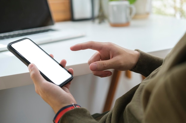 Feche a vista das mãos do jovem usando telefone inteligente enquanto está sentado no escritório em casa