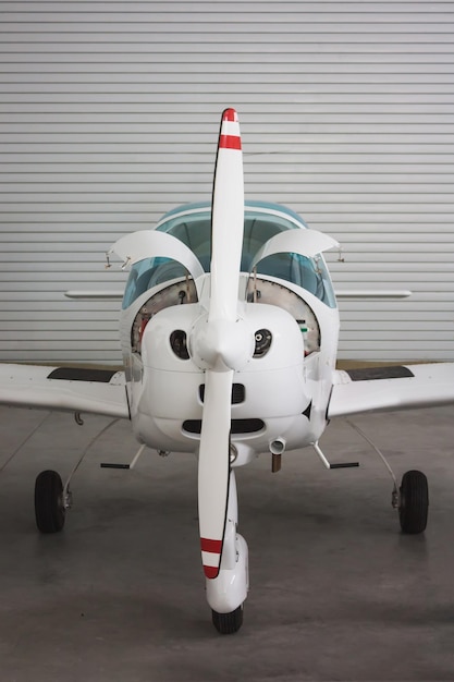 Feche a vista frontal de um pequeno avião esportivo branco em um hangar. A aeronave tem um motor aberto