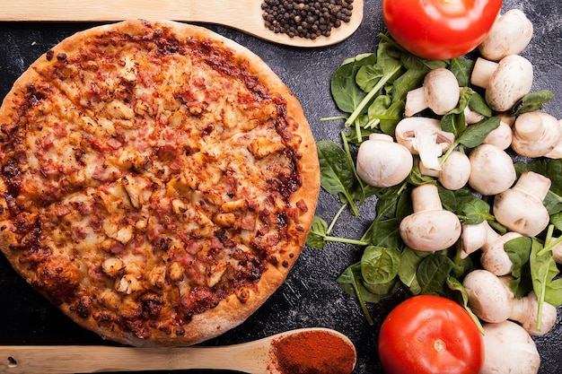 Foto feche a vista superior na pizza recém-assada ao lado dos ingredientes feitos na mesa de madeira escura