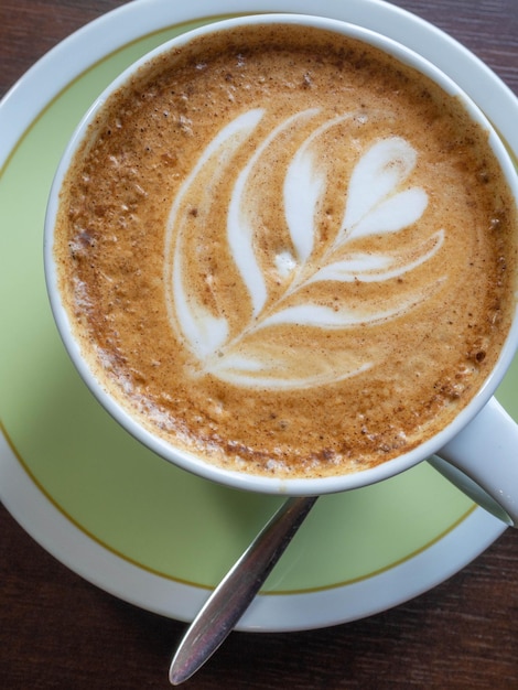 Feche a xícara de café branco com espuma de latte art em forma de mesa de madeira