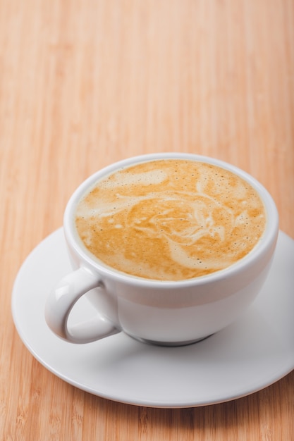 Feche a xícara de café branco com latte art na mesa de madeira no café