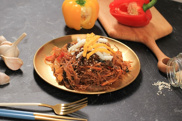 Feche acima da cozinha coreana autêntica, Japchae ou macarrão de vidro frito com legumes em placa de ouro. Coma diariamente ou no dia de Chuseok, copie o espaço no fundo preto