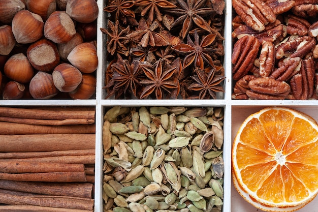 Feche acima da foto de cascas de canela, avelã, anis, nozes pecan, fatias de laranja seca e cardamomo.