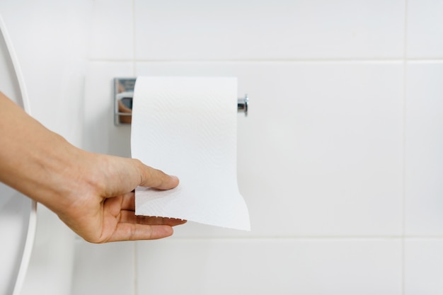Feche acima da mão asiática da mulher que puxa o papel no banheiro