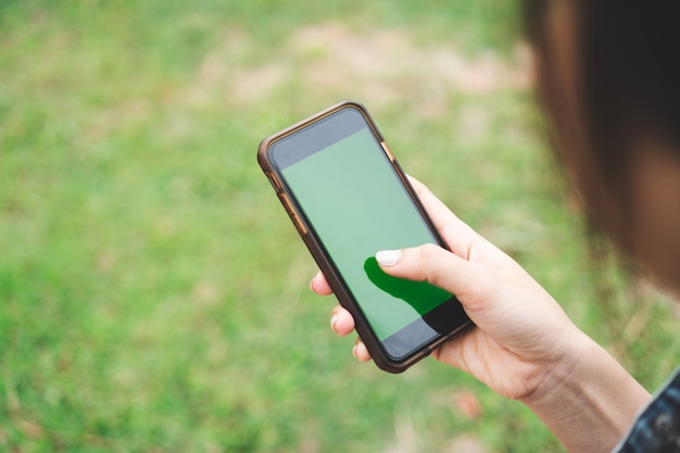 Feche acima da mão da mulher que guarda o smartphone com a tela verde vazia do espaço da cópia.