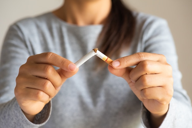 Feche acima da mão da mulher que quebra, esmagando ou destruindo cigarros no fundo preto.