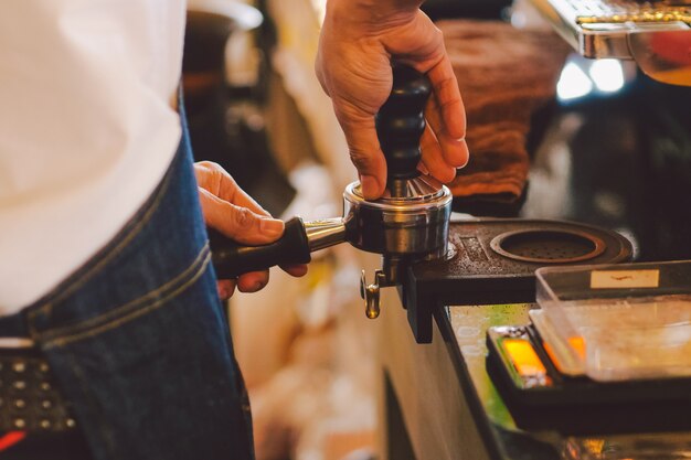 Feche acima da mão do barista que faz uma xícara de café.