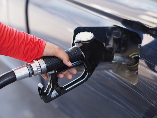 Feche acima da mão do homem que bombeia o combustível da gasolina no carro no posto de gasolina.