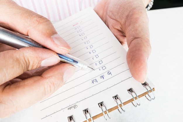 Feche acima da mão do homem que guarda e que escreve o caderno com letra para fazer a lista.