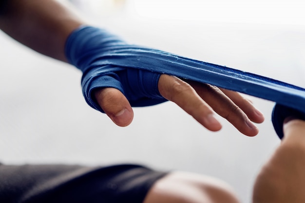 Feche acima da mão masculina do pugilista com as ataduras azuis do encaixotamento.