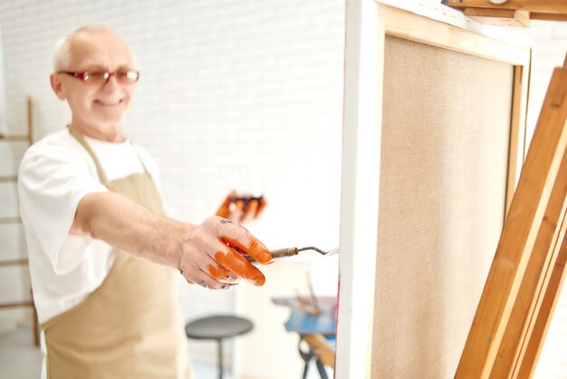 Feche acima da mão masculina sênior do pintor, pintando últimos cursos dentro, seus dedos todos que bordam na pintura alaranjada.