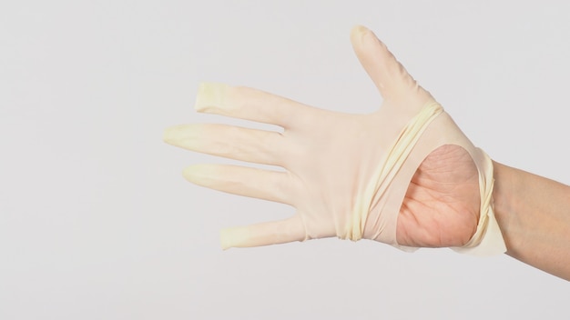 Feche acima da mão usando luvas médicas rasgadas ou luvas de borracha rasgadas em fundo branco.