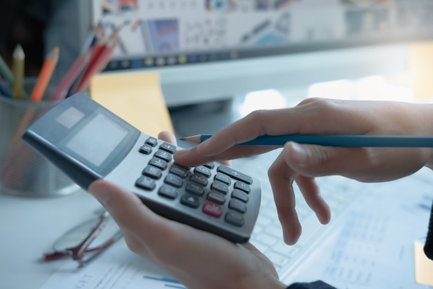 Feche acima da mulher de negócio que usa a calculadora e o portátil para fazem o financiamento da matemática na mesa de madeira no escritório e no fundo de trabalho do negócio