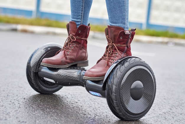 Feche acima da mulher que usa o hoverboard na estrada asfaltada. pés na scooter elétrica ao ar livre