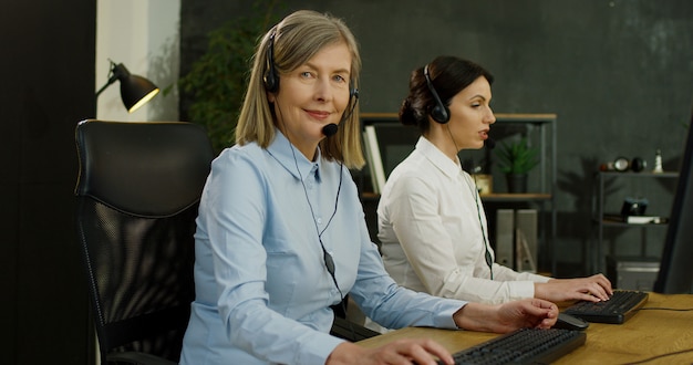 Feche acima da mulher sênior caucasiana no fone de ouvido trabalhando no escritório do call center. Serviço para o conceito de clientes.