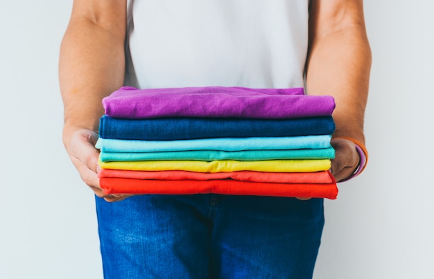 Foto feche acima da pilha de camisetas multicoloridas dobradas nas mãos