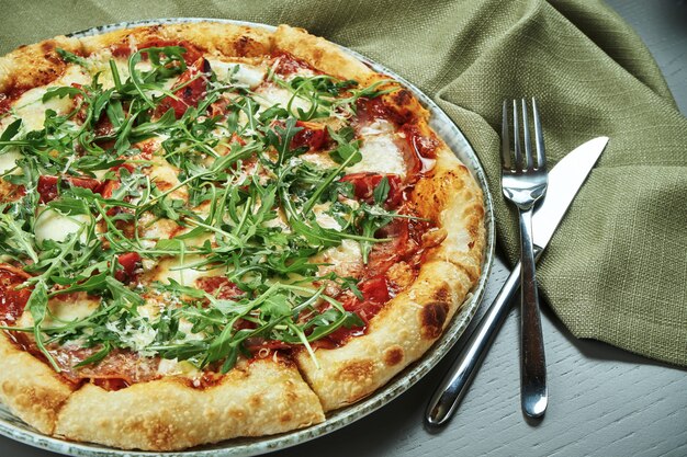 Feche acima da pizza apetitosa com presunto, rúcula, tomate, parmesão e mussarela na mesa de madeira em um restaurante. Foco seletivo, cópia de espaço