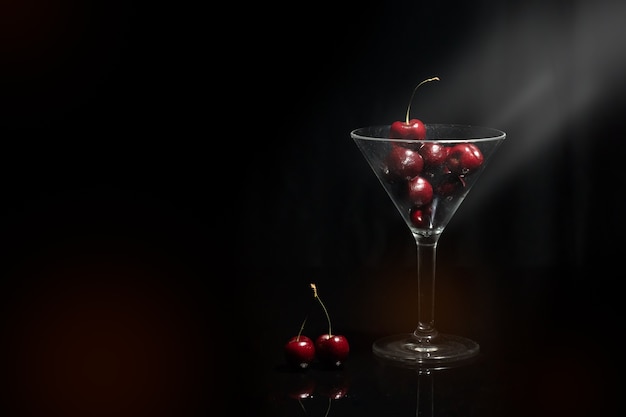 Feche acima da vista da cereja em um vidro de martini no fundo preto com alargamento e primeiro plano.