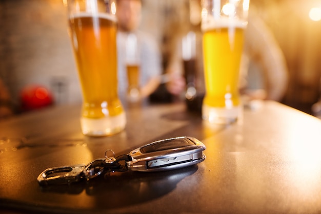 Feche acima da vista do foco das chaves do carro na mesa da barra na frente dos vidros com cerveja de pressão.