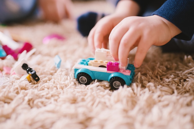 Foto feche acima da vista do foco de um carro de brinquedo plástico no tapete enquanto o garotinho mãos segurando-o.