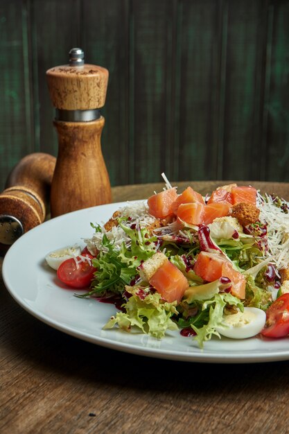 Feche acima da vista na salada Caesar servida com salmão defumado em chapa branca na superfície de madeira. Salada de frutos do mar saborosa. Vertical