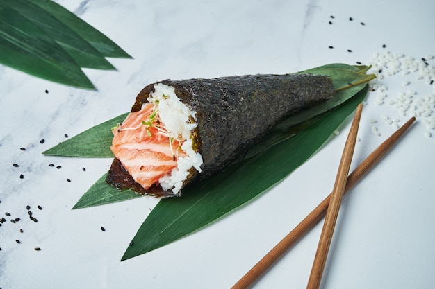 Feche acima da vista no fresco, sushi do temaki do marisco com salmões na superfície branca. Rolo de mão tradicional. Foco seletivo e horizontal