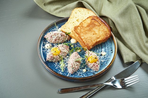 Feche acima da vista no tartare de carne fresca com pão, ovo e no prato. Vitela tartare caseira na mesa de madeira