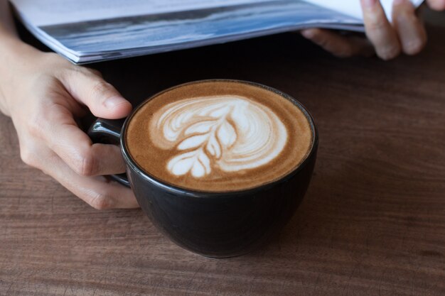 Feche acima da xícara de café quente da arte latte na mesa de madeira
