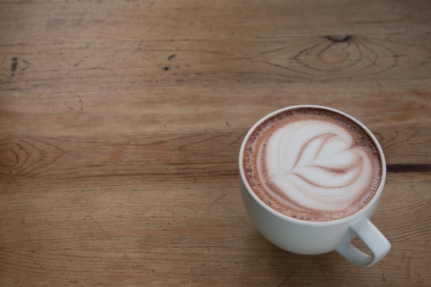 Feche acima da xícara de café quente da arte latte na mesa de madeira.