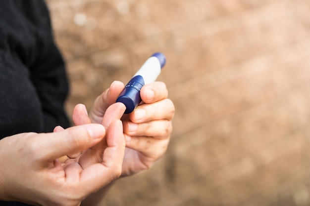 Feche acima das mãos da mulher usando a lanceta no dedo para verificar o nível do açúcar no sangue do diabetes.