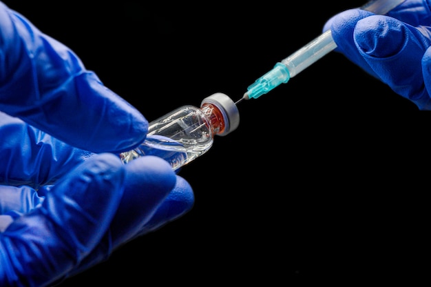 Feche acima das mãos do doutor que preparam a seringa e o tubo de ensaio, para a vacinação, no fundo isolado preto.