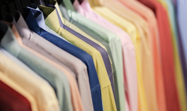 Feche acima das multi camisas coloridas em ganchos, fundo colorido de pano do vestuário