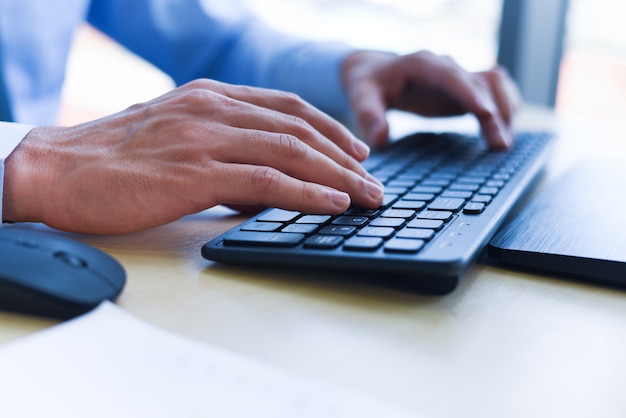 Feche acima de digitar a mão masculina no conceito de teclado - empresário trabalhando no teclado e mouse computador homem sentado na mesa e usando a tecnologia da internet no local de trabalho no escritório