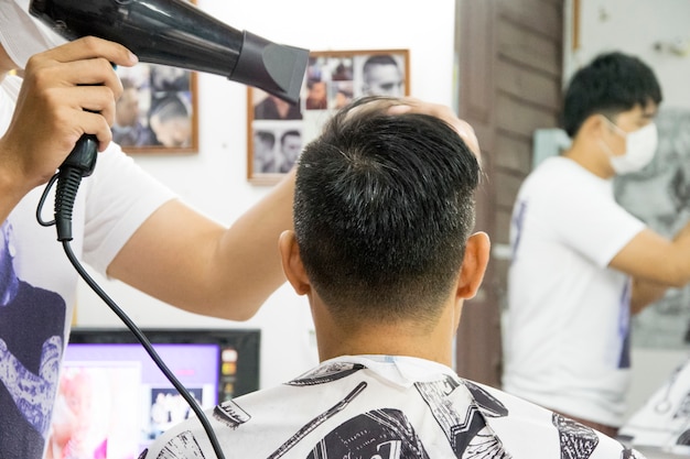 Feche acima de um cabeleireiro do homem com o secador de cabelo no barbeiro.