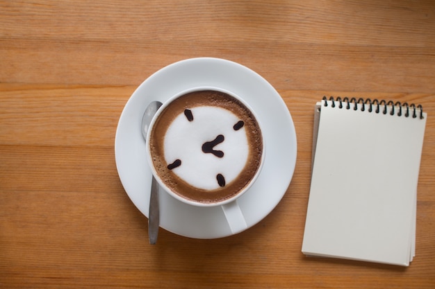 Foto feche acima de um café quente da arte do café de a cup desenhado um conceito do negócio do oclock na tabela de madeira com o livro de nota