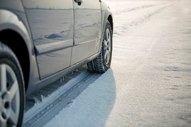 Feche acima de um pneu de carro estacionado na estrada nevado no dia de inverno. Transporte e segurança.