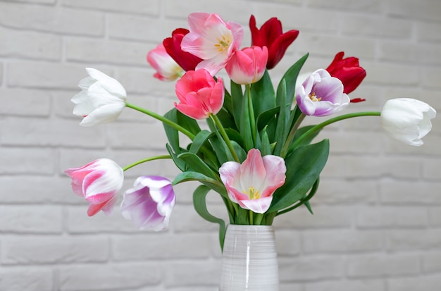 Feche acima de um ramalhete de tulipas bonitas em um vaso em uma parede de tijolos brancos.