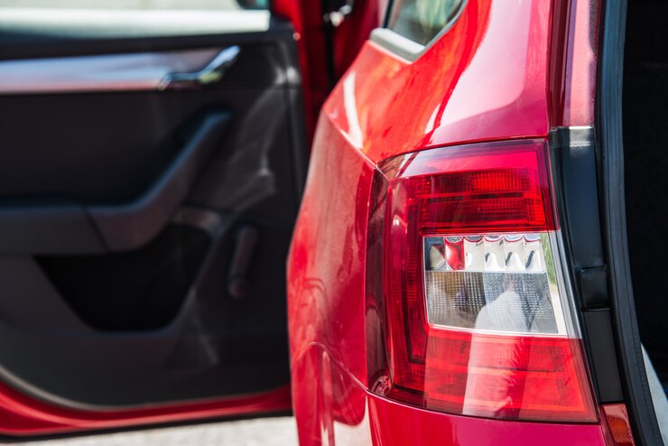 Foto feche acima de uma luz traseira do carro de um carro vermelho com a porta lateral aberta e o tronco.