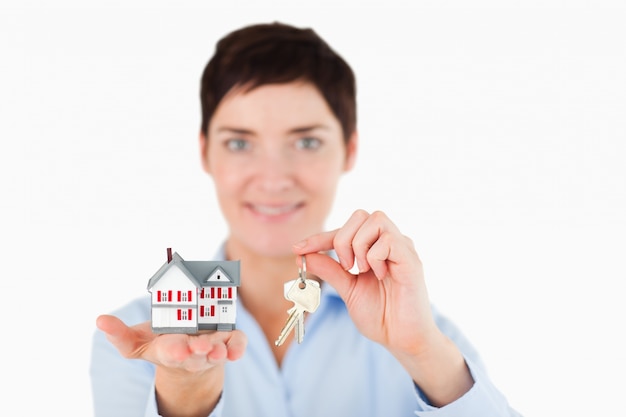 Feche acima de uma mulher que mostra chaves e uma casa em miniatura