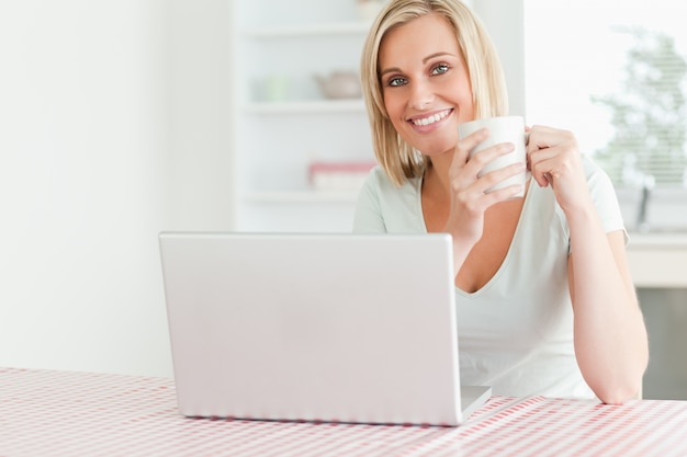 Feche acima de uma mulher segurando café com laptop na frente dela, sorrindo para a câmera
