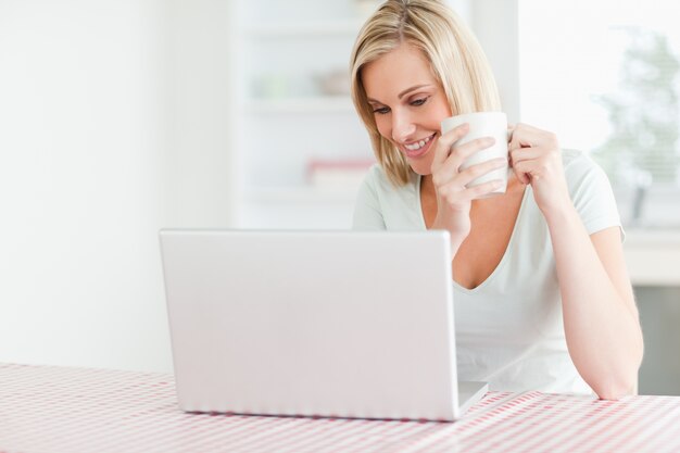 Feche acima de uma mulher segurando café olhando o laptop na frente dela