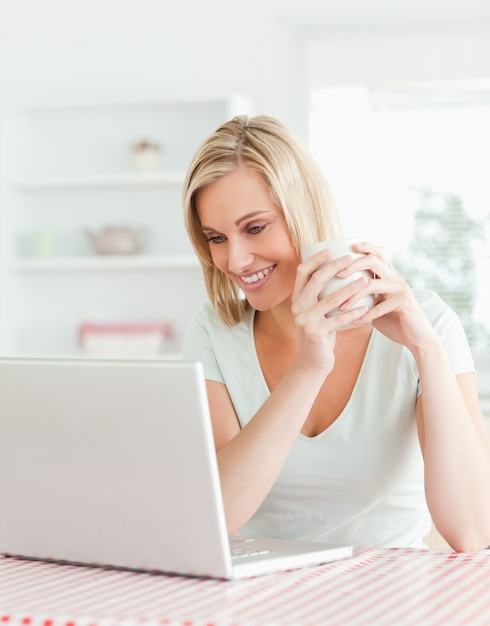 Feche acima de uma mulher segurando xícara de café olhando o laptop na frente dela