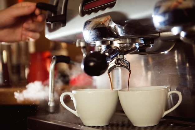 Feche acima do café que derrama da máquina do café nos copos brancos.