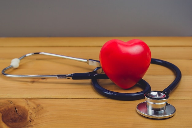 Feche acima do coração vermelho e steythoscope na tabela de madeira velha