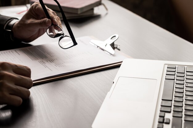 Feche acima do homem de negócios que guarda monóculos e que lê originais na mesa de escritório.