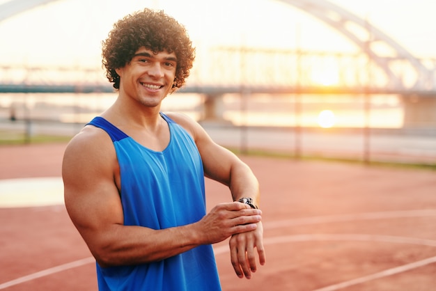 Feche acima do homem desportivo que ajusta o relógio esperto ao estar na corte na manhã.