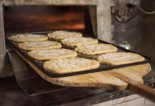 Feche acima do padeiro que põe na pastelaria fresca do forno.