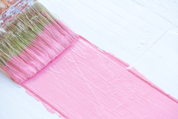 Feche acima do pincel que pinta a cor cor-de-rosa em uma tabela de madeira branca.
